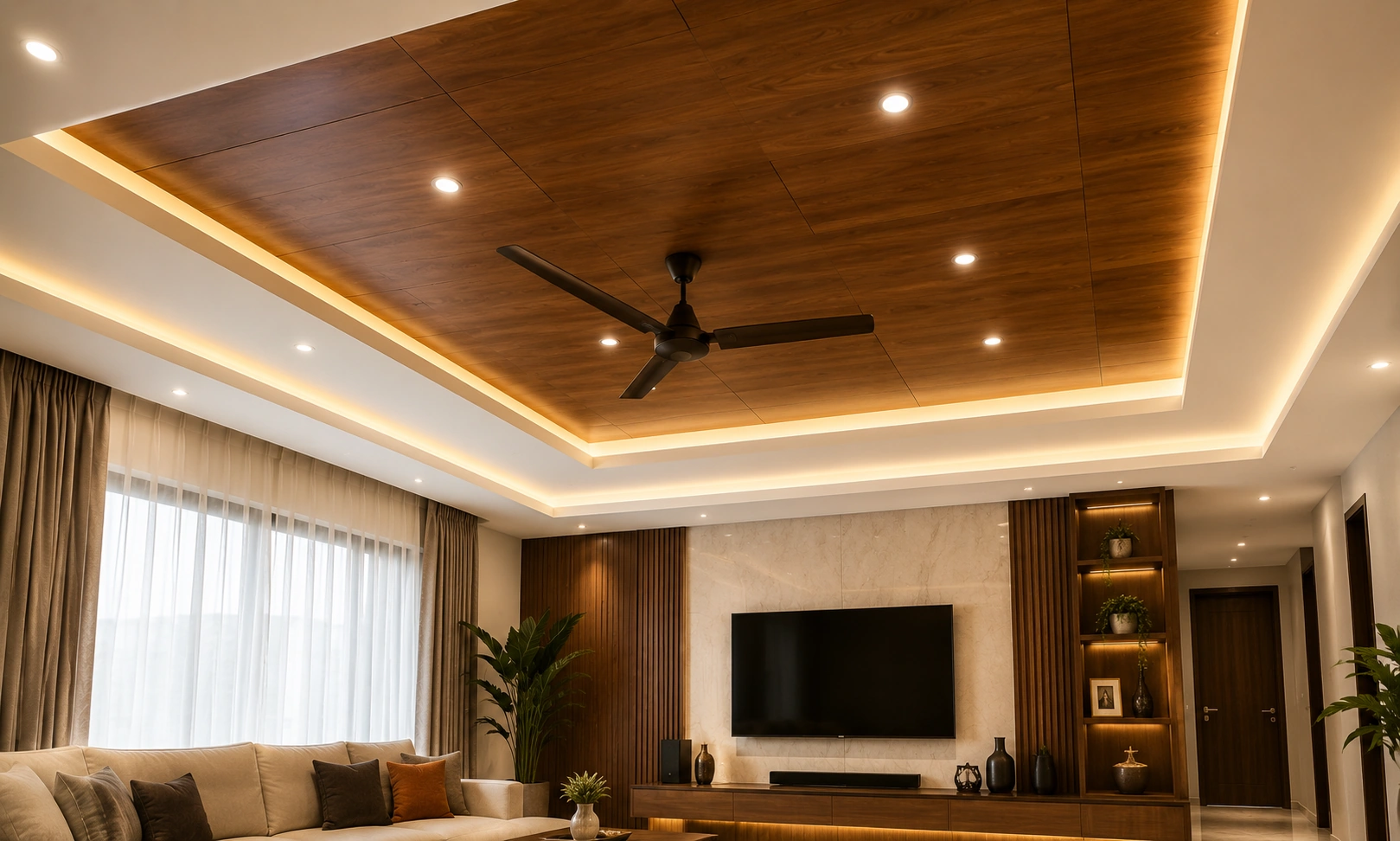 Modern wooden false ceiling with warm LED cove lighting, recessed spotlights, and ceiling fan designed by False Ceiling Interior Designers in Trivandrum.