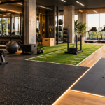 Modern gym interior featuring rubber flooring, artificial turf, wood flooring, and cushioned workout areas for different training zones.